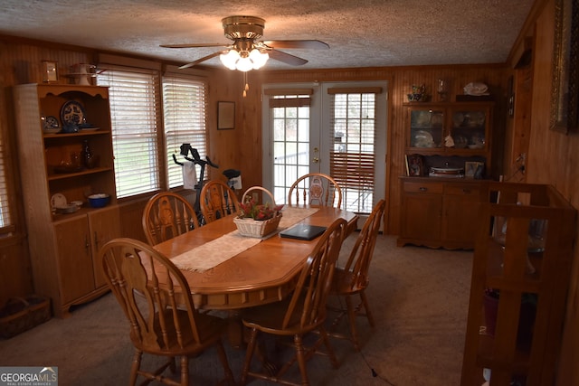 carpeted dining area featuring a textured ceiling, wooden walls, ceiling fan, and french doors