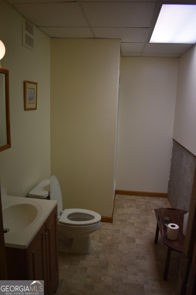 bathroom with a paneled ceiling, toilet, and vanity