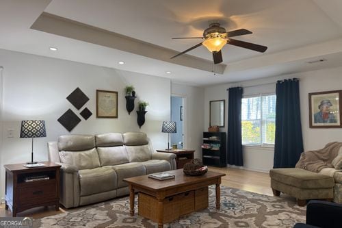 living room featuring ceiling fan, light wood-type flooring, and a tray ceiling