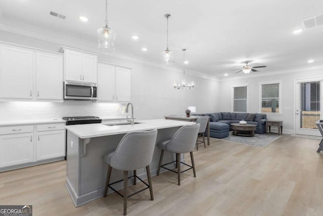 kitchen with sink, white cabinetry, hanging light fixtures, ornamental molding, and an island with sink