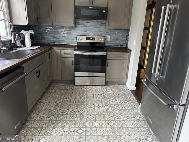 kitchen featuring appliances with stainless steel finishes, a sink, gray cabinetry, wooden counters, and backsplash