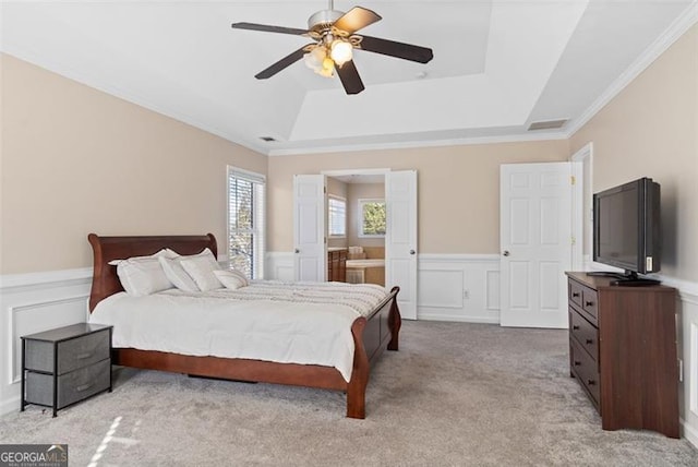 carpeted bedroom with a raised ceiling, crown molding, connected bathroom, and ceiling fan