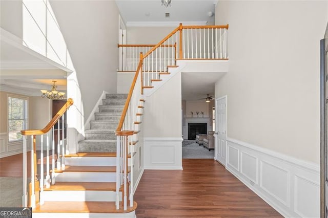 stairway with crown molding, ceiling fan with notable chandelier, and hardwood / wood-style flooring