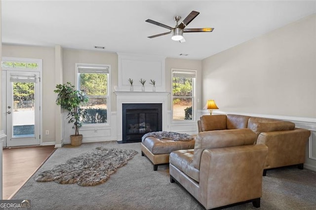 living room with a large fireplace, dark wood-type flooring, and ceiling fan