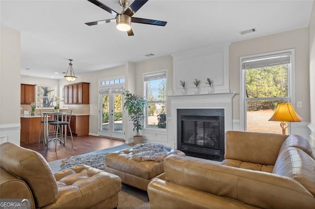 living room featuring ceiling fan, a fireplace, dark hardwood / wood-style flooring, and french doors