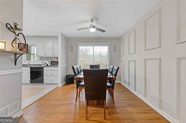 dining space with sink, ceiling fan, light hardwood / wood-style flooring, and a textured ceiling