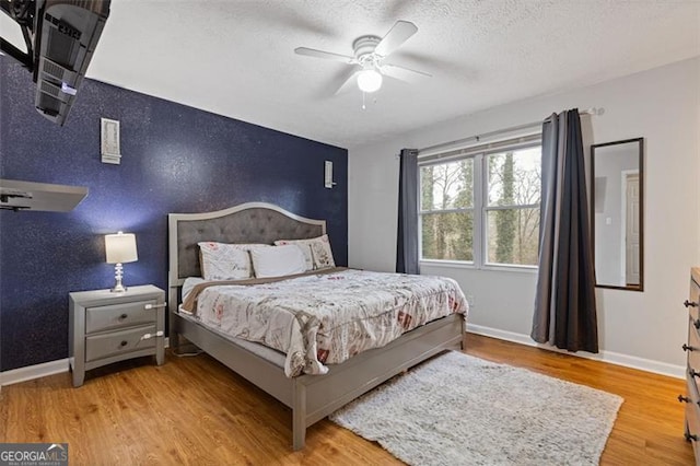 bedroom with ceiling fan, light hardwood / wood-style flooring, and a textured ceiling