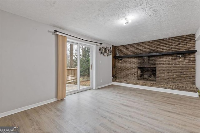 unfurnished living room with brick wall, a brick fireplace, light hardwood / wood-style flooring, and a textured ceiling