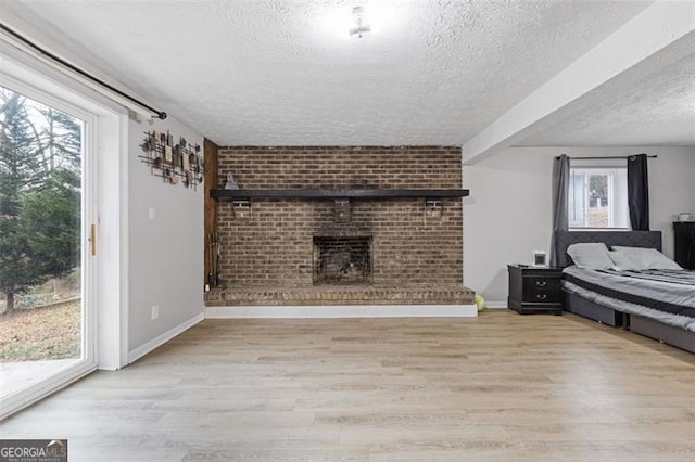 bedroom with light hardwood / wood-style floors, a textured ceiling, a brick fireplace, and access to outside