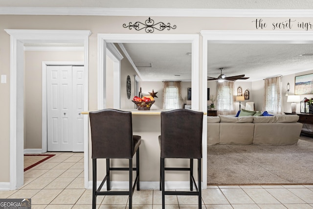 kitchen with a textured ceiling, light tile patterned floors, ornamental molding, ceiling fan, and a breakfast bar area