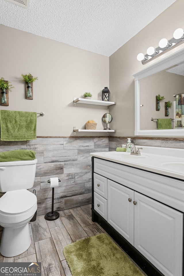 bathroom with a textured ceiling, toilet, vanity, and tile walls