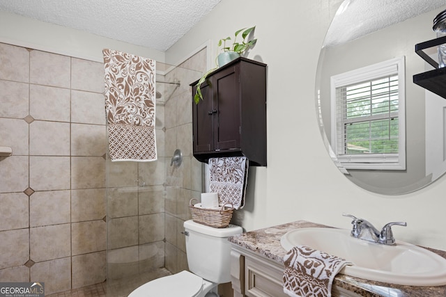 bathroom featuring a textured ceiling, toilet, vanity, and tiled shower