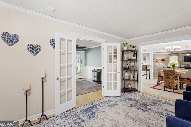 interior space with wood-type flooring, french doors, a textured ceiling, ornamental molding, and a chandelier