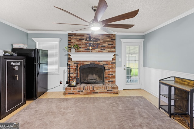 living room featuring crown molding, light hardwood / wood-style flooring, ceiling fan, a fireplace, and a textured ceiling