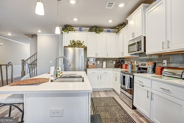 kitchen featuring decorative light fixtures, white cabinetry, a center island with sink, and appliances with stainless steel finishes