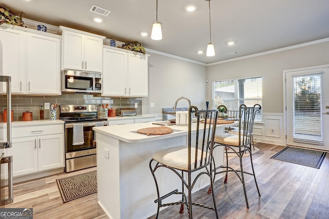 kitchen with decorative light fixtures, sink, white cabinets, a center island with sink, and stainless steel appliances