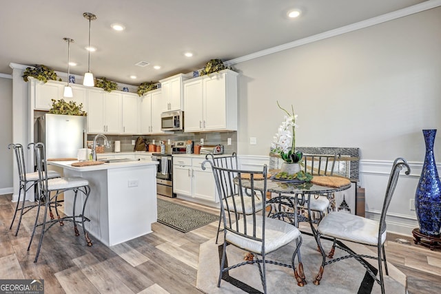 kitchen featuring sink, decorative light fixtures, a kitchen island with sink, light hardwood / wood-style floors, and stainless steel appliances