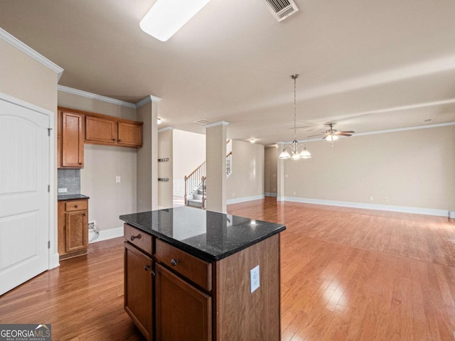 kitchen featuring dark stone countertops, hanging light fixtures, a center island, ornamental molding, and decorative backsplash