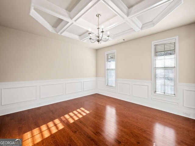 empty room featuring a wealth of natural light, hardwood / wood-style floors, a notable chandelier, and coffered ceiling