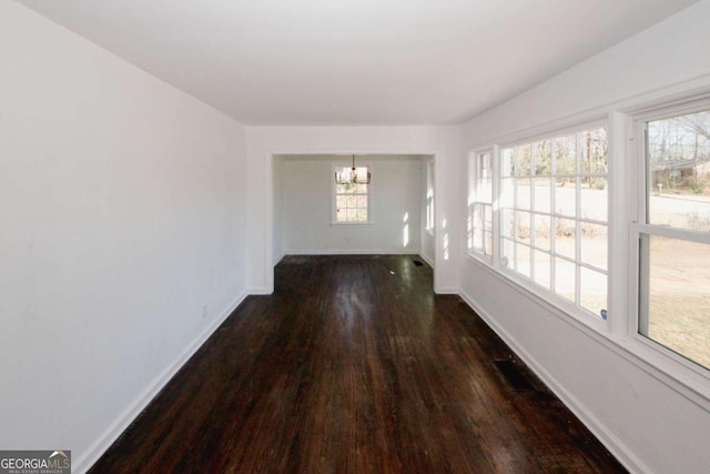 unfurnished dining area featuring dark wood-type flooring, a chandelier, and a healthy amount of sunlight