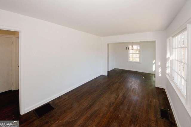 empty room with a notable chandelier and dark hardwood / wood-style floors