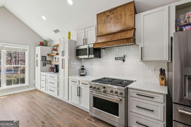 kitchen with light hardwood / wood-style floors, white cabinetry, decorative backsplash, stainless steel appliances, and lofted ceiling