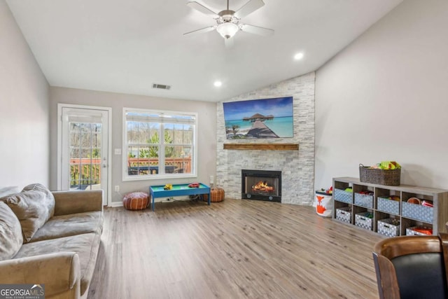 living room with wood-type flooring, ceiling fan, a fireplace, and lofted ceiling