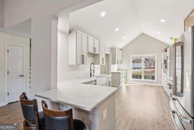 kitchen with kitchen peninsula, a kitchen breakfast bar, sink, light wood-type flooring, and high end refrigerator