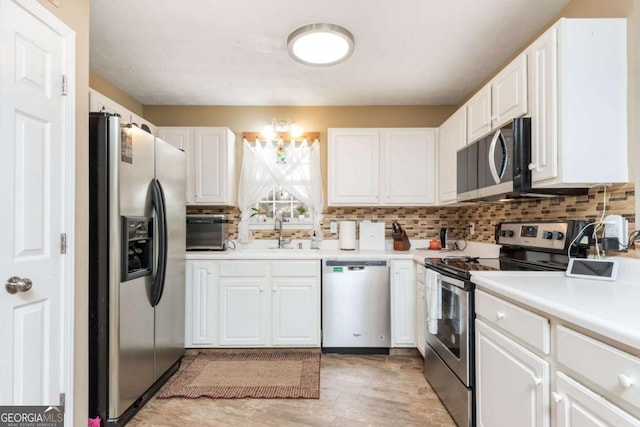 kitchen with appliances with stainless steel finishes, sink, white cabinets, light hardwood / wood-style floors, and decorative backsplash