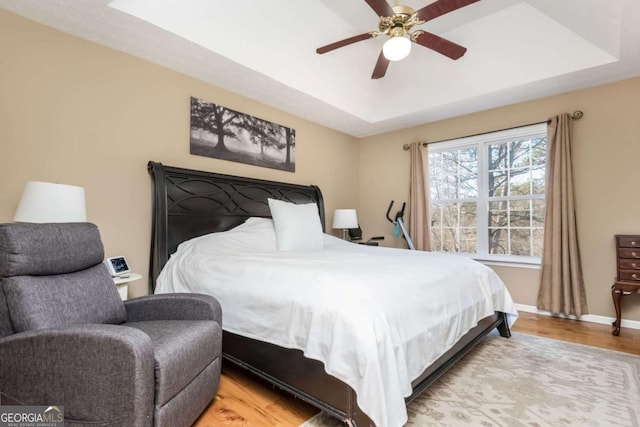 bedroom with ceiling fan, a raised ceiling, and light hardwood / wood-style flooring