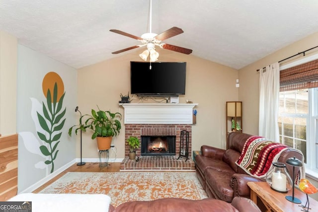 living room with hardwood / wood-style floors, a textured ceiling, ceiling fan, vaulted ceiling, and a brick fireplace