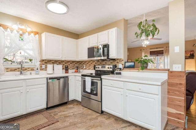 kitchen featuring kitchen peninsula, sink, white cabinets, decorative backsplash, and stainless steel appliances