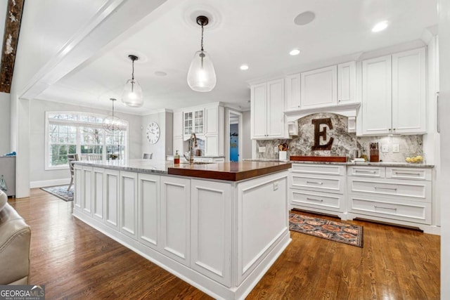 kitchen with decorative backsplash, white cabinetry, a center island with sink, and pendant lighting