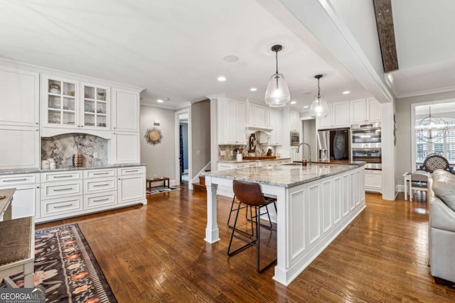 kitchen featuring backsplash, white cabinetry, a kitchen island with sink, and hanging light fixtures