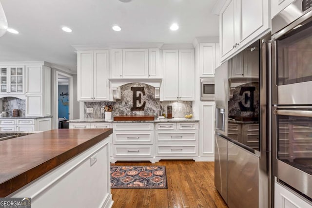 kitchen featuring white cabinets, dark wood-type flooring, stainless steel appliances, dark stone countertops, and backsplash