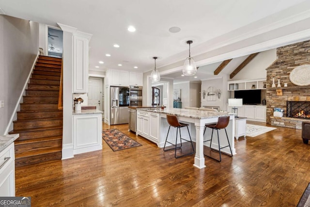 kitchen with appliances with stainless steel finishes, a kitchen island with sink, white cabinets, pendant lighting, and light stone counters