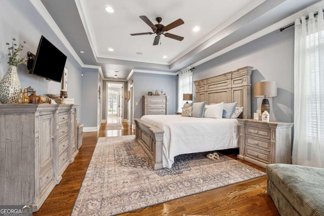 bedroom with ceiling fan, a raised ceiling, ornamental molding, and dark wood-type flooring