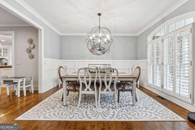 dining area with wood-type flooring, ornamental molding, and a notable chandelier