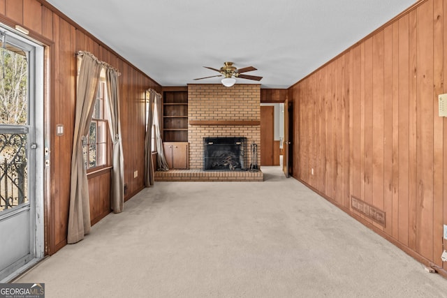 unfurnished living room with built in shelves, light colored carpet, a fireplace, and ceiling fan