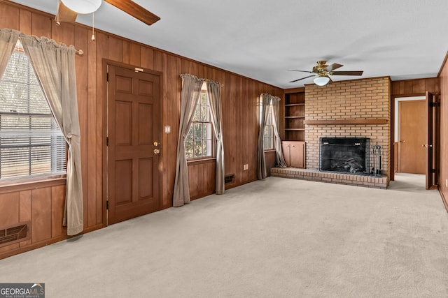 unfurnished living room with light carpet, a brick fireplace, wood walls, and ceiling fan