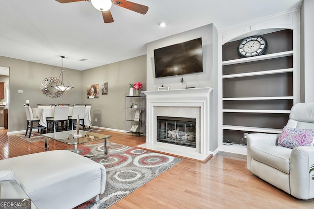 living room with ceiling fan, built in shelves, and light wood-type flooring