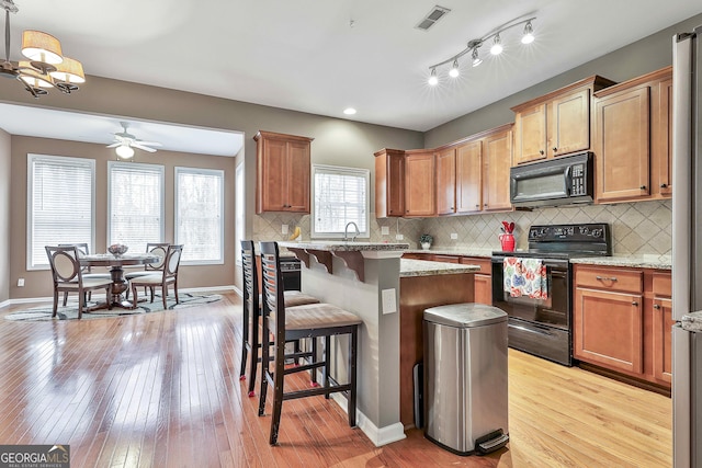 kitchen with black appliances, a center island, a kitchen breakfast bar, backsplash, and light stone counters