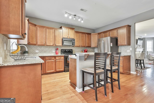 kitchen featuring black appliances, a kitchen bar, light hardwood / wood-style flooring, backsplash, and light stone counters