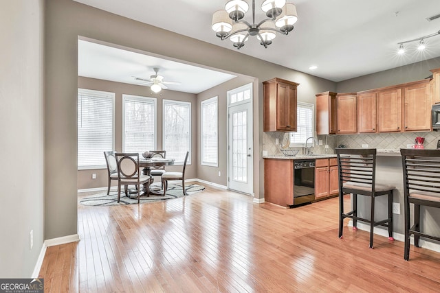 kitchen featuring black dishwasher, hanging light fixtures, light hardwood / wood-style flooring, backsplash, and ceiling fan with notable chandelier