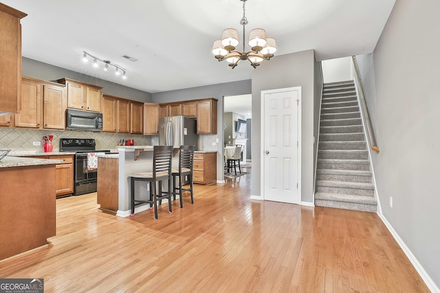 kitchen featuring black appliances, tasteful backsplash, hanging light fixtures, light hardwood / wood-style flooring, and a breakfast bar area