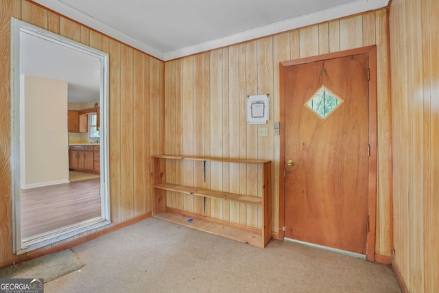 foyer entrance featuring light colored carpet, wooden walls, and crown molding