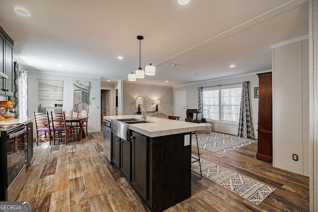 kitchen with appliances with stainless steel finishes, dark hardwood / wood-style floors, sink, crown molding, and a center island with sink