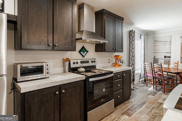 kitchen with stainless steel appliances, dark brown cabinets, wall chimney range hood, and light hardwood / wood-style flooring