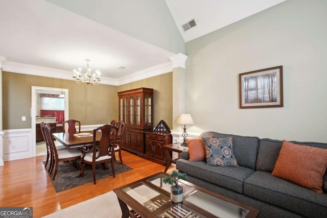 living room featuring hardwood / wood-style flooring, crown molding, an inviting chandelier, and ornate columns