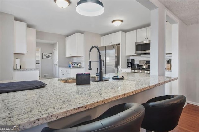 kitchen featuring light stone countertops, decorative backsplash, a kitchen breakfast bar, white cabinets, and stainless steel appliances